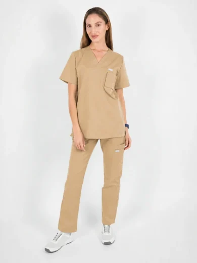 Woman in beige medical scrubs standing with hands at her sides, wearing white sneakers, in a studio setting.
