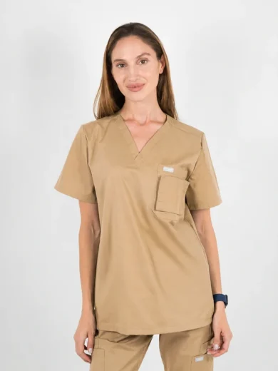 Woman wearing tan medical scrubs with a chest pocket, standing against a light background.