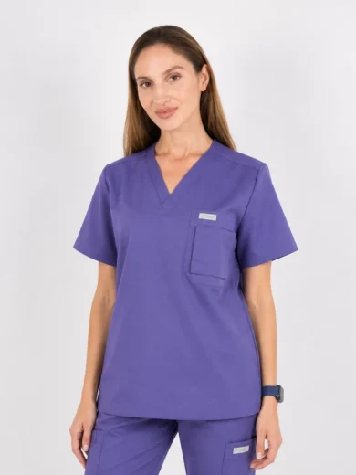 Woman wearing purple medical scrubs with a V-neck top and chest pocket, standing against a light background.