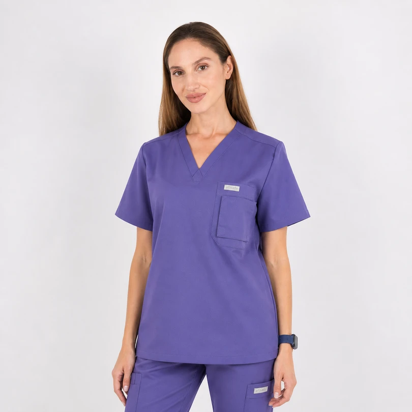 Woman wearing purple medical scrubs with a V-neck top and chest pocket, standing against a light background.
