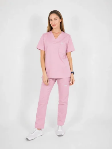 Woman wearing pink scrubs with V-neck top and matching pants, standing against a light background.