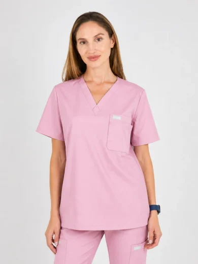 Woman wearing pink medical scrubs with V-neck top and matching pants, standing and smiling in a neutral setting.