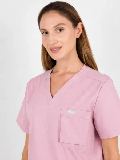 Female model wearing pink medical scrubs with a front chest pocket against a light background only.