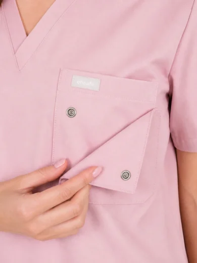 Close-up of a pink medical scrub top with a chest pocket being opened, showing a flap and metal snap buttons.