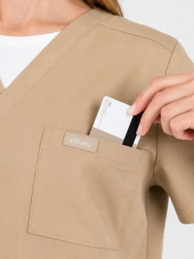 Beige scrub top with a front chest pocket holding a card in place.