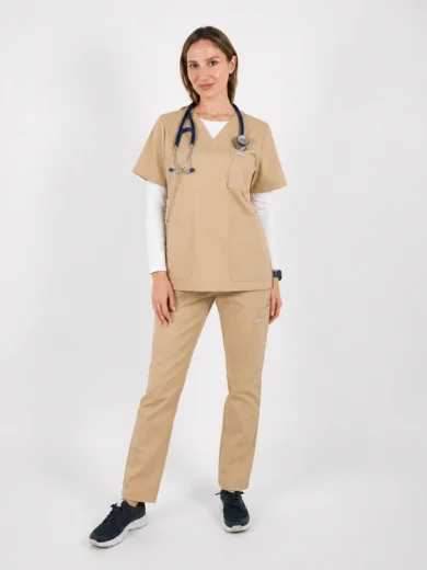 Female healthcare worker in beige scrubs with a stethoscope around her neck, standing and smiling.
