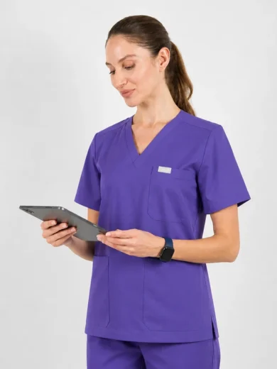 Female healthcare professional in purple scrubs using a tablet while standing