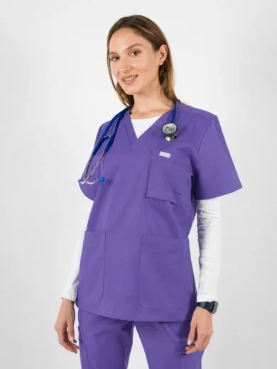 Female healthcare worker in purple scrubs with stethoscope around her neck, standing and smiling.