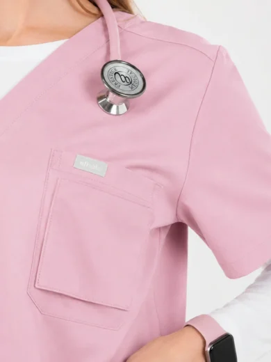 Pink medical scrubs top with chest pocket, stethoscope draped over shoulder, white undershirt visible at the neckline, and a smartwatch on the wrist.