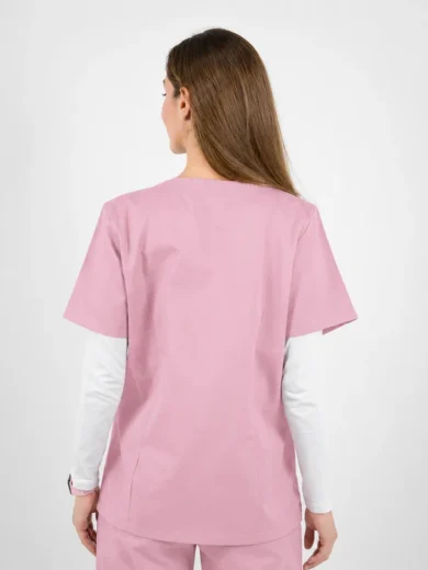 Back view of a person wearing light pink medical scrubs with a white long-sleeve shirt underneath, standing against a neutral background.
