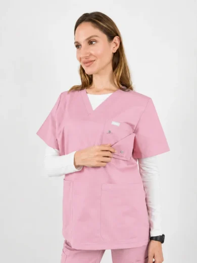 Female healthcare worker wearing pink scrubs with a white undershirt, holding the chest pocket and looking to the side.