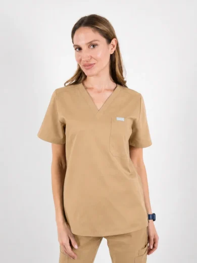 Woman in tan medical scrubs standing against a white background, hands at sides, wearing a smartwatch on her left wrist.