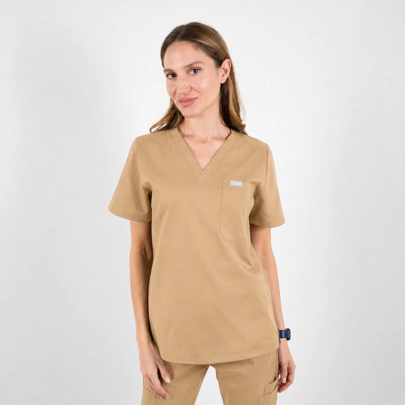 Woman in tan medical scrubs standing against a white background, hands at sides, wearing a smartwatch on her left wrist.