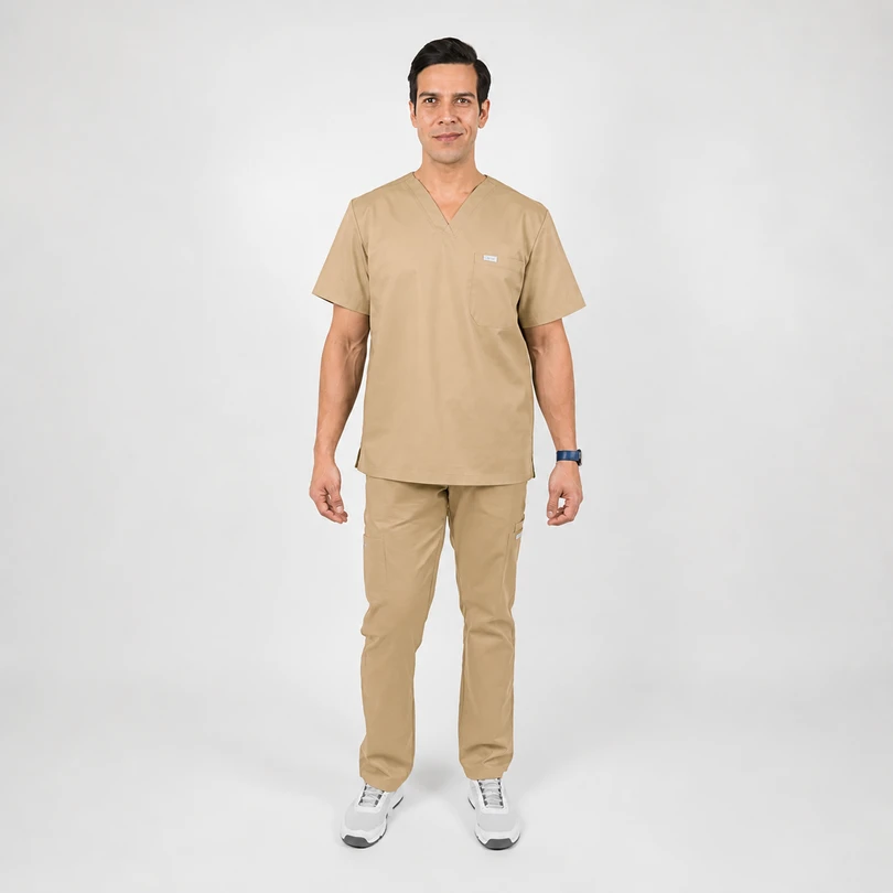 Man wearing tan medical scrubs (top and pants) standing and facing the camera in a neutral studio.