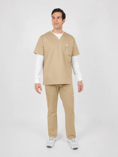 Man wearing beige medical scrubs with a white long-sleeve undershirt, standing and looking slightly to the side in a neutral studio setting.