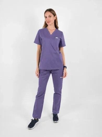 Woman in purple medical scrubs standing against a white background, smiling slightly.