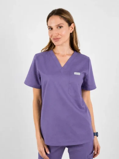 Woman in purple medical scrubs with a V-neck top and chest pocket, standing against a light background.