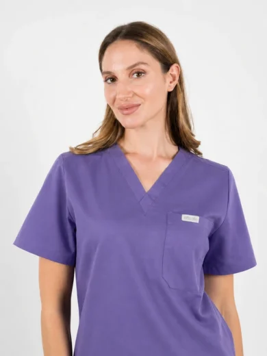 Model wearing a purple medical scrubs top with a V-neck and left chest pocket, facing the camera.