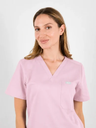 Woman wearing light pink scrubs with V-neck, facing slightly to the left, smiling against a neutral background.