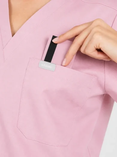 Close-up of a pink medical scrub top pocket with a small black-and-white safety device being tucked in by a gloved or bare hand.