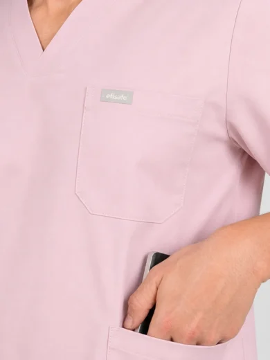 Light pink medical scrubs with a chest pocket and a hand placing a phone in the lower pocket.