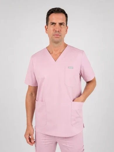 Man wearing light pink medical scrubs with a V-neck top and two front pockets, standing against a gray background.
