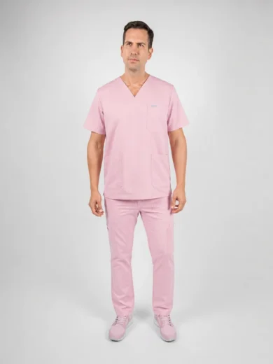Man wearing pink medical scrubs standing facing the camera in a studio backdrop with a neutral gray background.] ,
