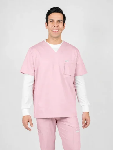 Smiling man in light pink scrubs with white undershirt standing against a neutral backdrop.