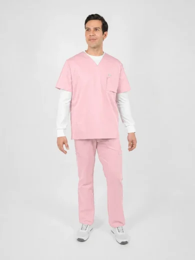 Man wearing pink scrub top and pants with a white undershirt, standing in a neutral studio backdrop.
