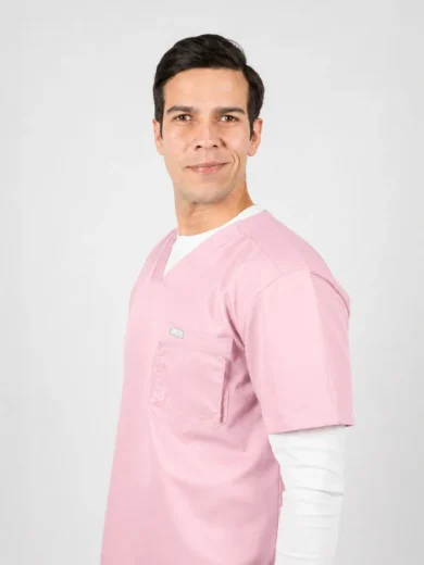 Man in pink scrubs posing in profile against a light gray background, smiling at the camera.