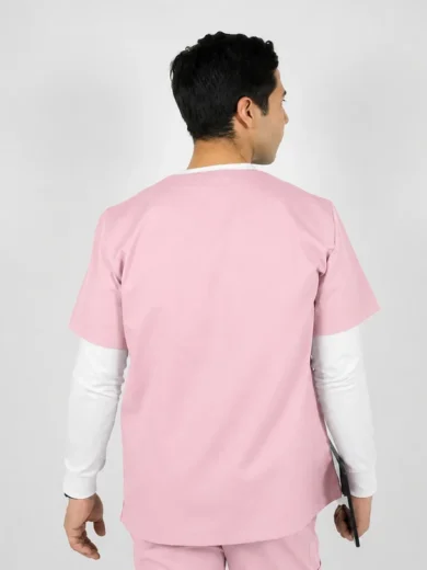 Person in pink scrubs seen from the back, holding a clipboard in one hand, white long-sleeve shirt underneath, neutral background
