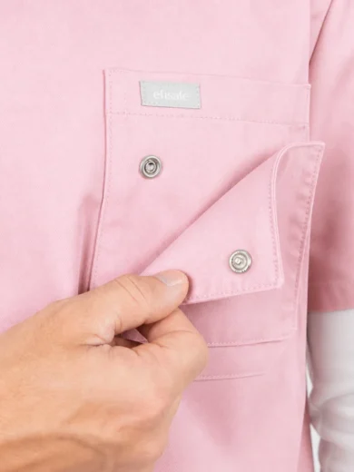 Person adjusting the flap of a pink shirt pocket with metal snap buttons, close-up detail.