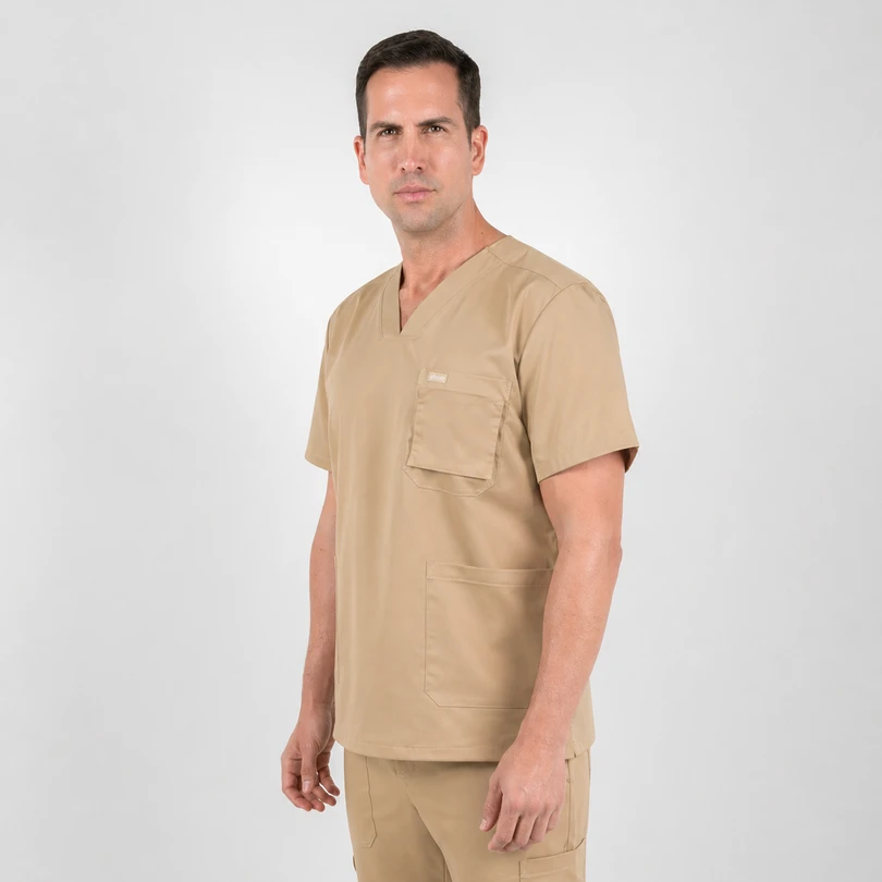 Adult man in tan medical scrubs stands against a light gray background, facing slightly to the right with a neutral expression.