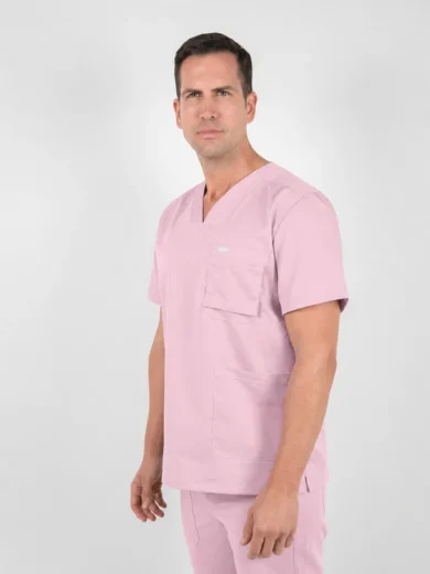 Man wearing light pink medical scrubs standing in a studio, facing slightly to the right.