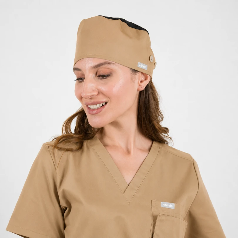 Woman in beige medical scrubs and matching cap, smiling and looking to her left.