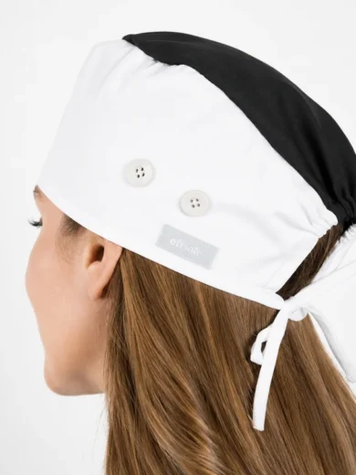 Rear view of a white and black scrub cap with two buttons, tied with a white ribbon at the back on a person with long hair.