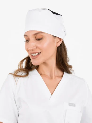 Smiling woman in white medical scrubs and cap, looking to her left against a clean white background.