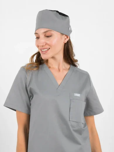 Woman in gray medical scrubs and matching cap, smiling and looking to the side.