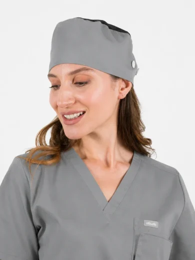 Female healthcare professional wearing gray scrubs and a matching cap, smiling and looking to the side.