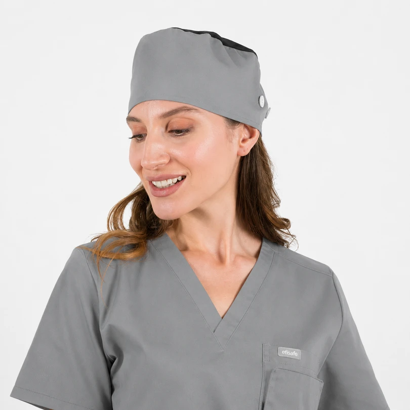 Female healthcare professional wearing gray scrubs and a matching cap, smiling and looking to the side.