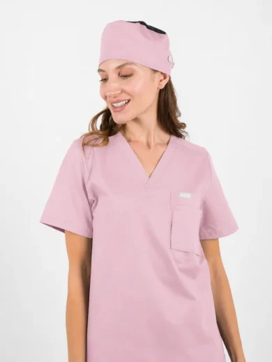 Woman in light pink scrubs with V-neck top and chest pocket, wearing a matching pink scrub cap and looking to the side.