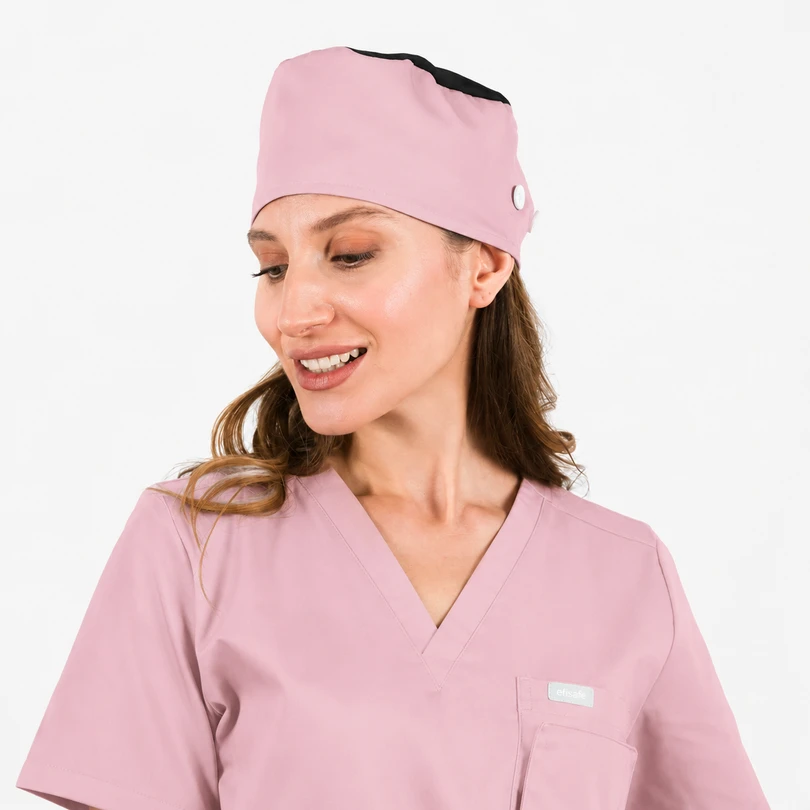 Woman in pastel pink scrubs and matching scrub cap, smiling and looking to her left.