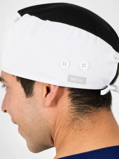 Side view of a man wearing a white surgical cap with a black top and a small brand label on the band.