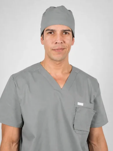 Male surgeon in gray scrubs and cap, looking at the camera with a neutral expression.