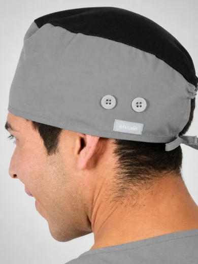 Profile view of a man wearing a gray surgical cap with a black top, featuring two white buttons and a small tag.
