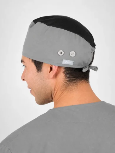 Profile view of a man wearing a two-tone gray surgical cap with a small tag and tie at the back, against a light background.