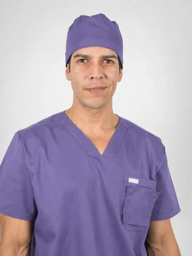 Male healthcare professional in purple scrubs and cap, facing the camera with a neutral expression.