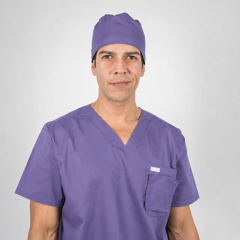 Male healthcare professional in purple scrubs and cap, facing the camera with a neutral expression.