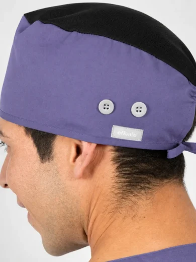 Side view of a purple surgical cap with a black top, worn by a person; two small white buttons and a tied back strap visible.