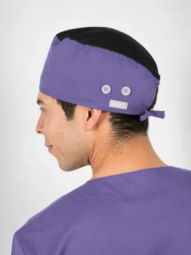 Side view of a person wearing a purple surgical cap with a black top and matching scrubs, viewed from behind-left.